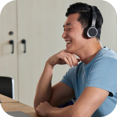 Person at a desk, smiling and wearing noise cancelling headphones