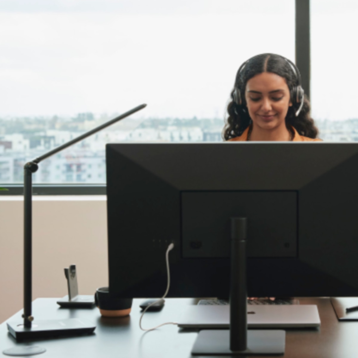 A contact center agent wearing a work headset stands behind a monitor.