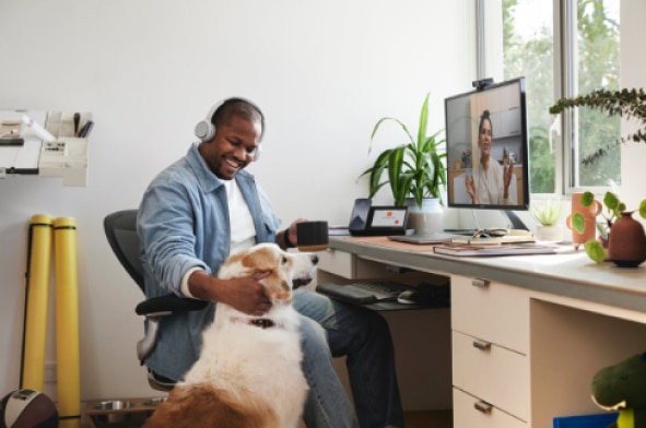 A person pets a dog while participating in a hybrid work virtual meeting.