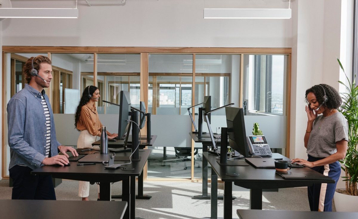 a team of three colleagues, each at a standing desk, use VoIP