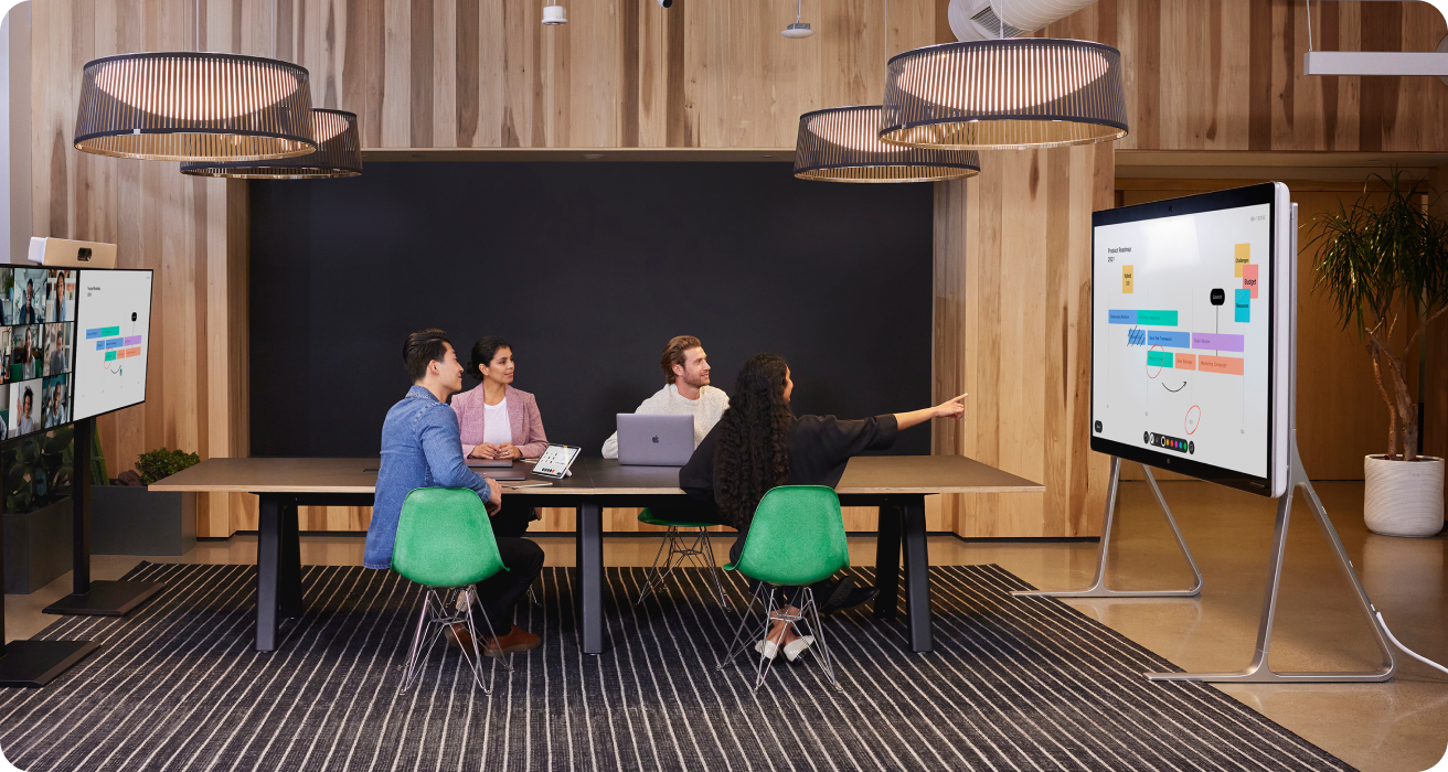 4 people holding a live conference with a large digital whiteboard holding their attention