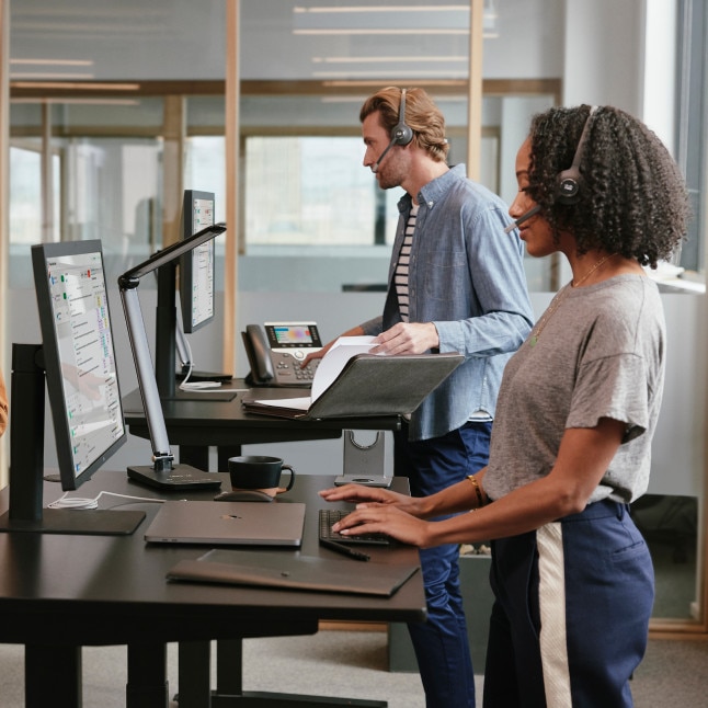 two people working at standing desks, looking like they may be on calls