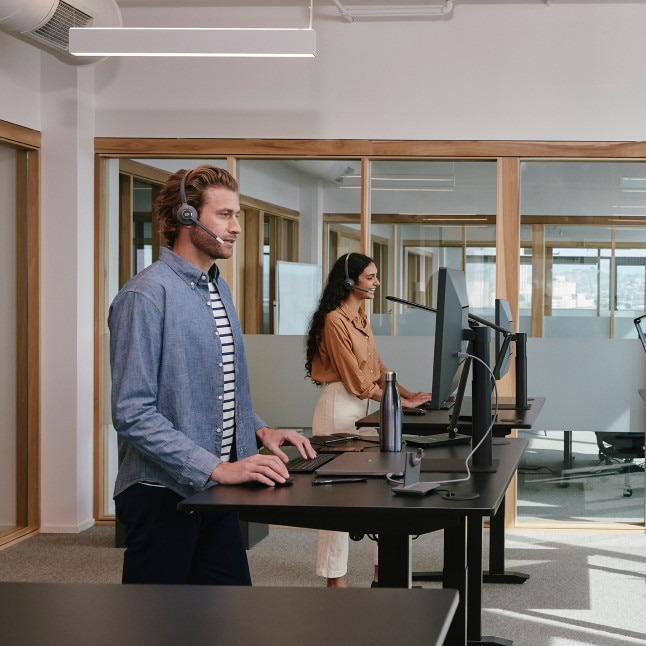 two people working at standing desks, looking busy and possibly on calls