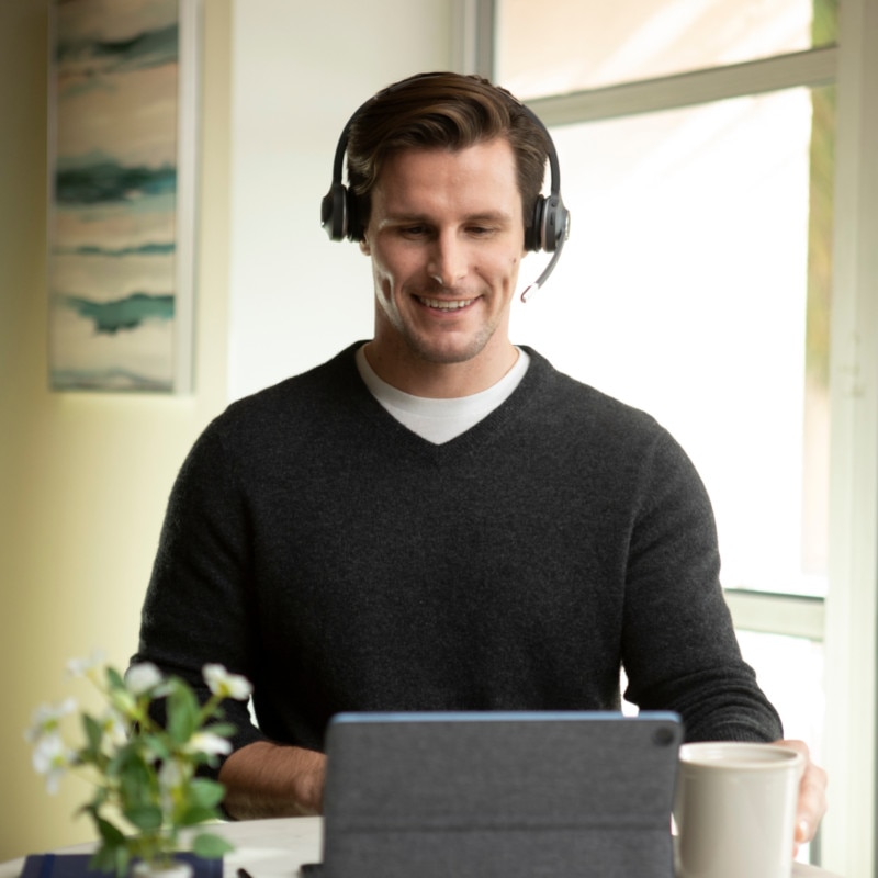 A smiling contact center agent in a headset helps a customer while working from home.