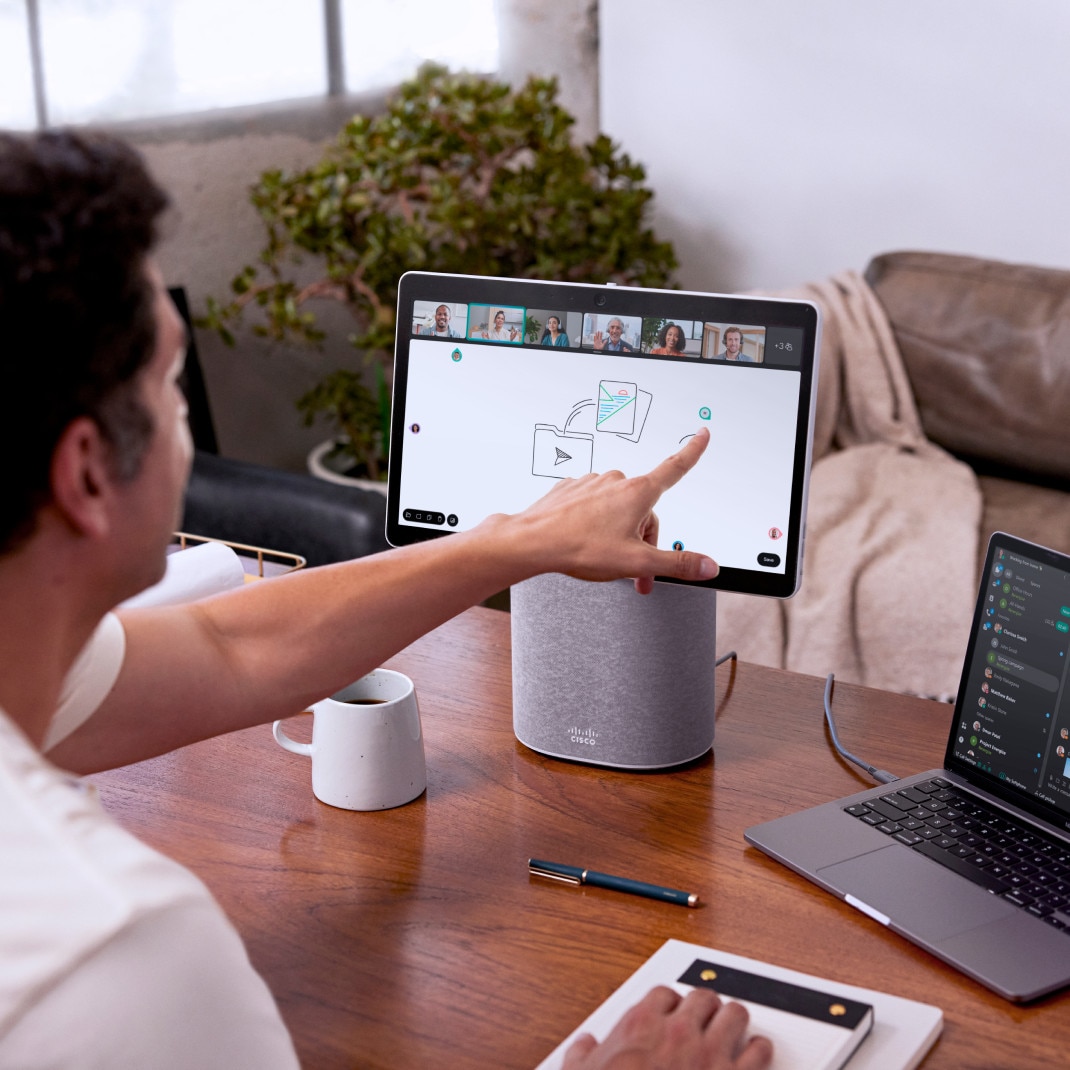 A professional in a home office collaborates with several colleagues via a Webex video meeting on a Webex Desk Mini.