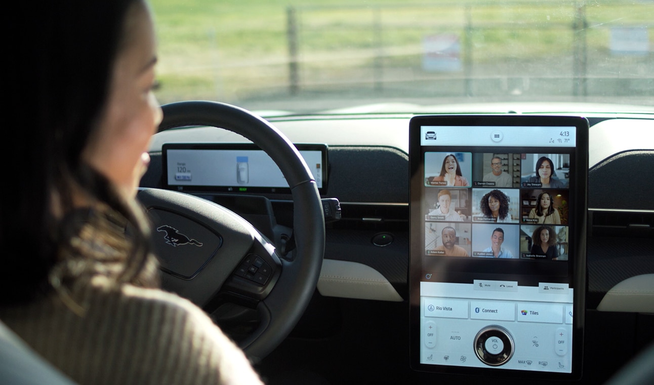 Driver uses Ford dashboard to display grid view Webex video conference with in-office and remote workers.
