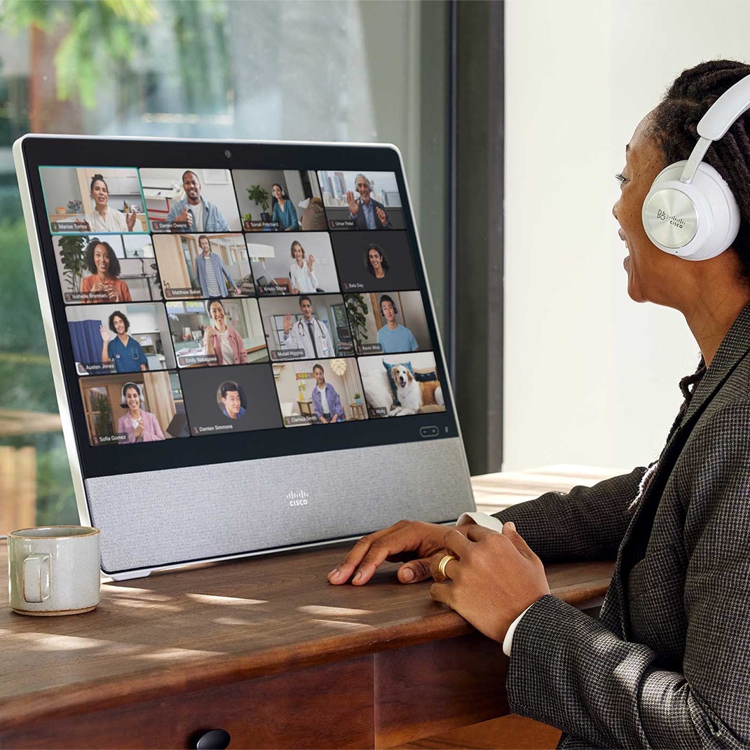 Remote worker uses Cisco Desk Pro for Webex video conference in grid view.