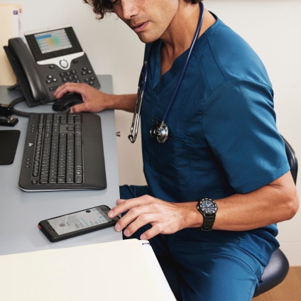 Busy looking medical worker at desk with mobile phone, desk phone, keyboard, and mouse