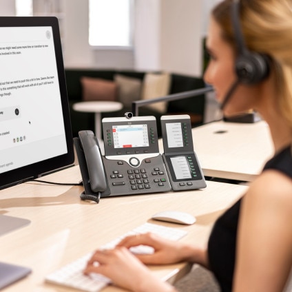 Person working at desk with PC monitor and Cisco IP phone prominently displayed