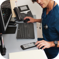 Busy looking medical worker at desk with mobile phone, desk phone, keyboard, and mouse