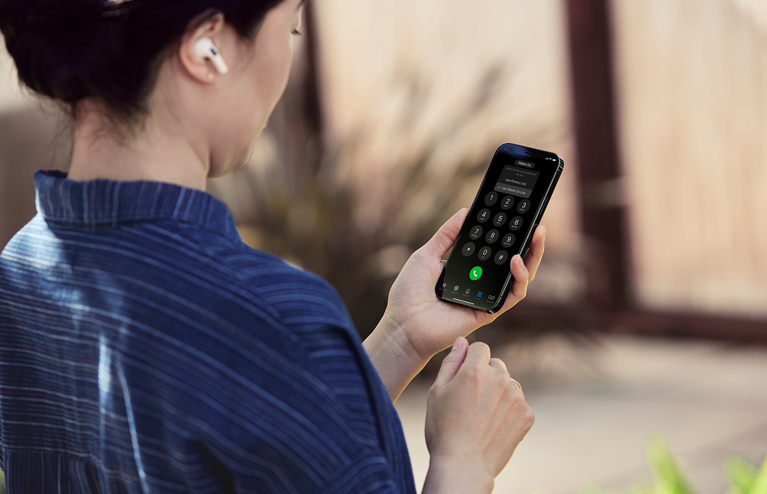 Person in a blue striped shirt looks at the number pad of a mobile device.