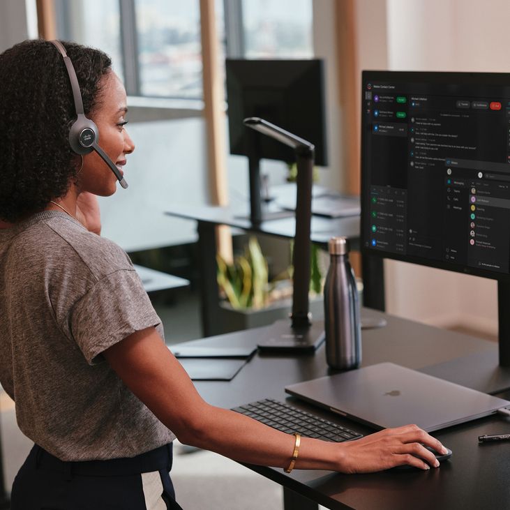 A contact center agent works at a standing desk with Webex Contact Center open on her computer screen.