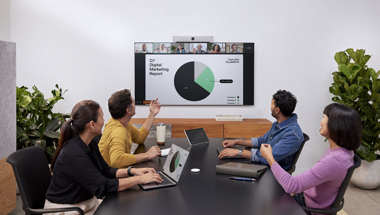 A team in a conference room reviewing a "Q1 Digital Marketing Report" pie chart on a large wall-mounted display.
