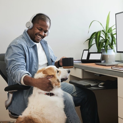 A smiling person working remotely in a home office, pausing to pet his dog.