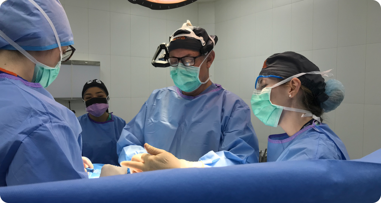 Surgeon in RealWear headset stands with 3 other medical professionals, leveraging Webex Expert on Demand during a surgery.