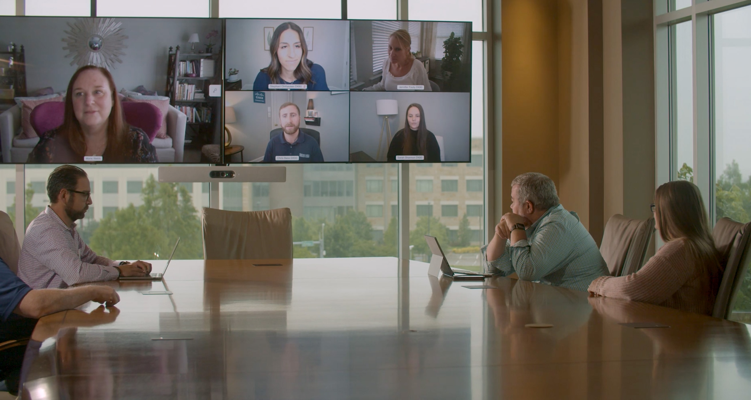 The team collaborates via a video meeting, with some people joining from a conference room and others from other locations.