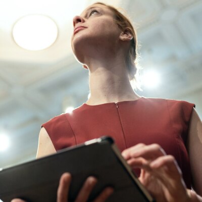 A person dressed in bergundy holds a tablet while looking into the distance.