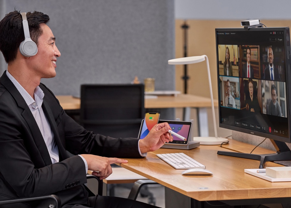 A smiling professional wearing headphones has an online meeting with six other people.