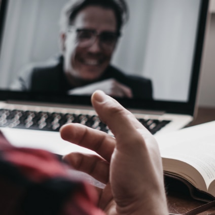 A hand is seen gesturing at a person smiling on a laptop screen.