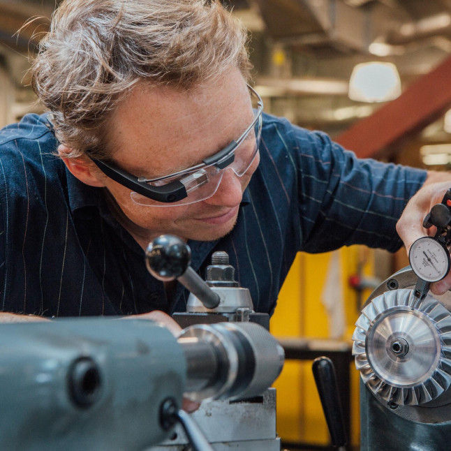 A frontline worker wearing a RealWear Headset works on some machinery, leveraging Webex Expert on Demand.