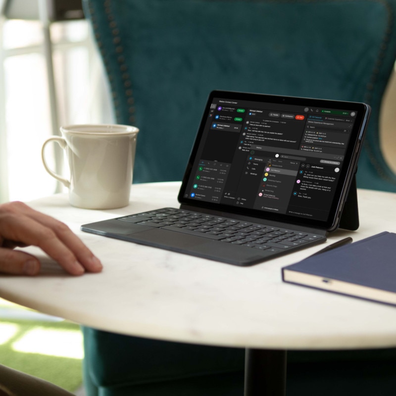 A tablet displaying the Webex Contact Center interface sits on a table in an employee's home workspace.